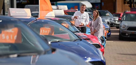 A salesman and lady talking on a car lot