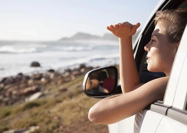 Young person parked on the beach in a car and shielding the sun from their eyes