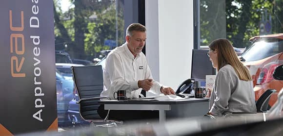 RAC Approved Dealer salesman and lady sat at a desk in a showroom