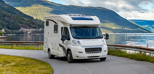 White motorhome on the road with a lake behind it
