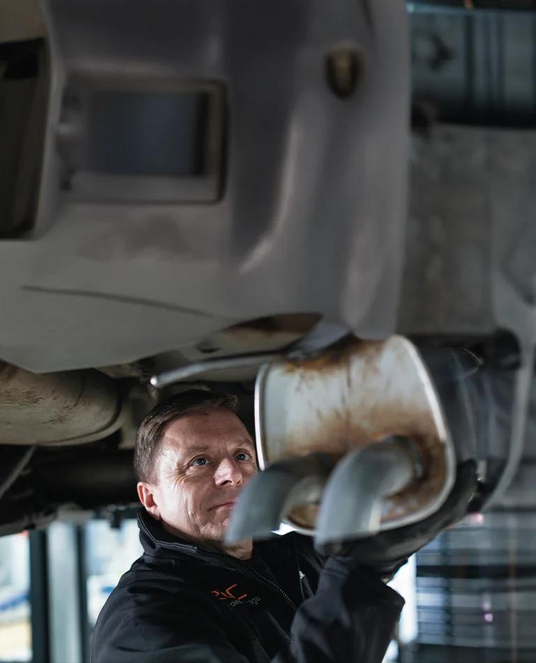 A mechanic inspecting the exhaust of a car vehicle.