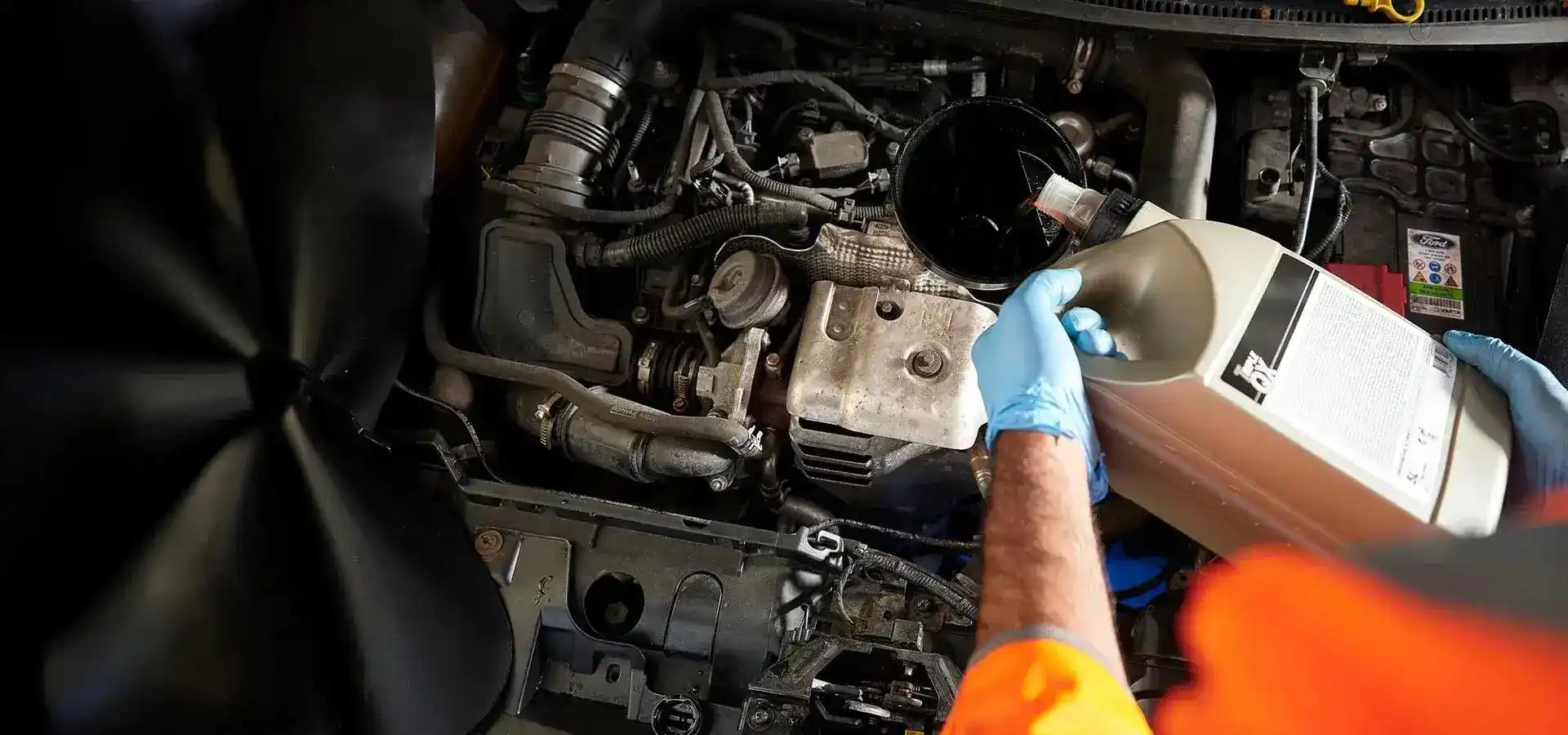 A mechanic topping up a car vehicles oil.