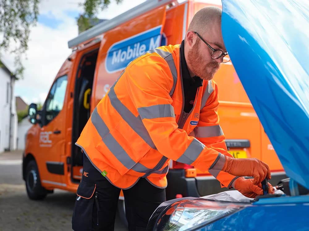 A close up of an RAC mobile mechanic looking under the hood of a car