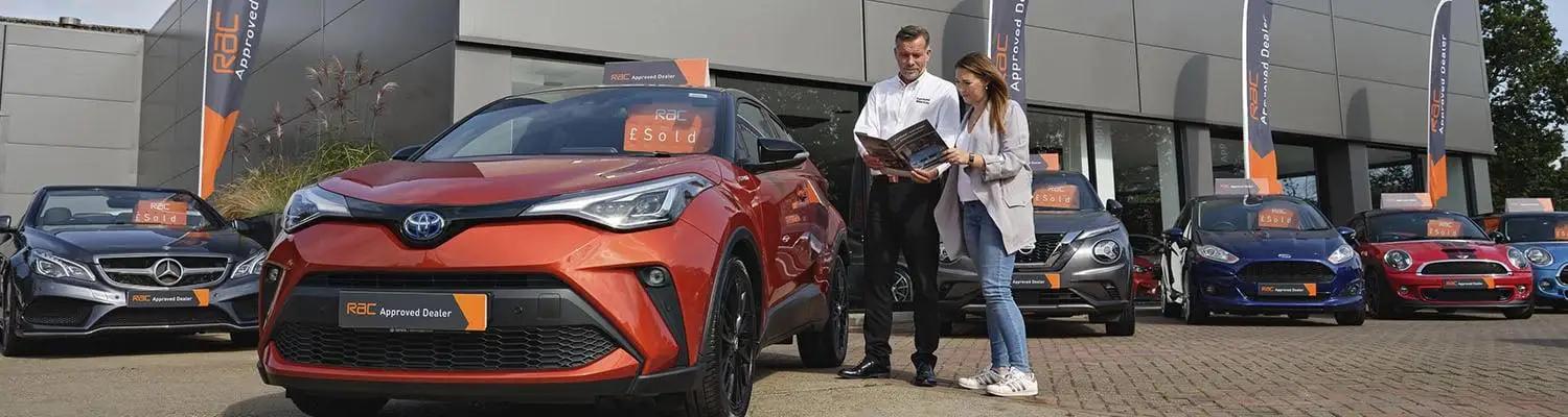 A lady talking to a salesman outside of a car showroom