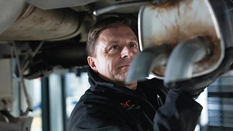 A mechanic under a car raised on a vehicle bay